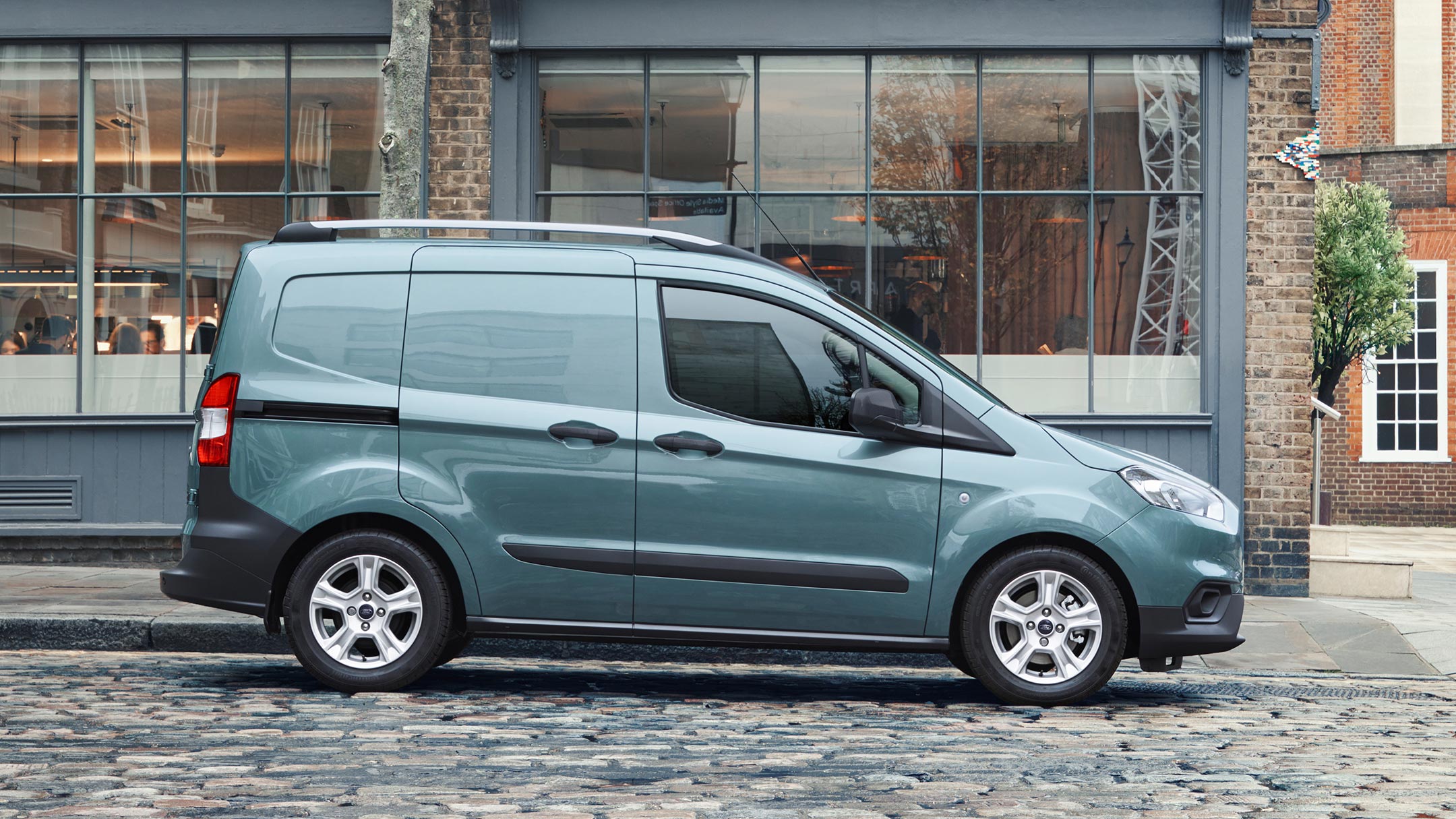 Ford Transit Courier Blau Seitenansicht parkt vor modernem Gebäude