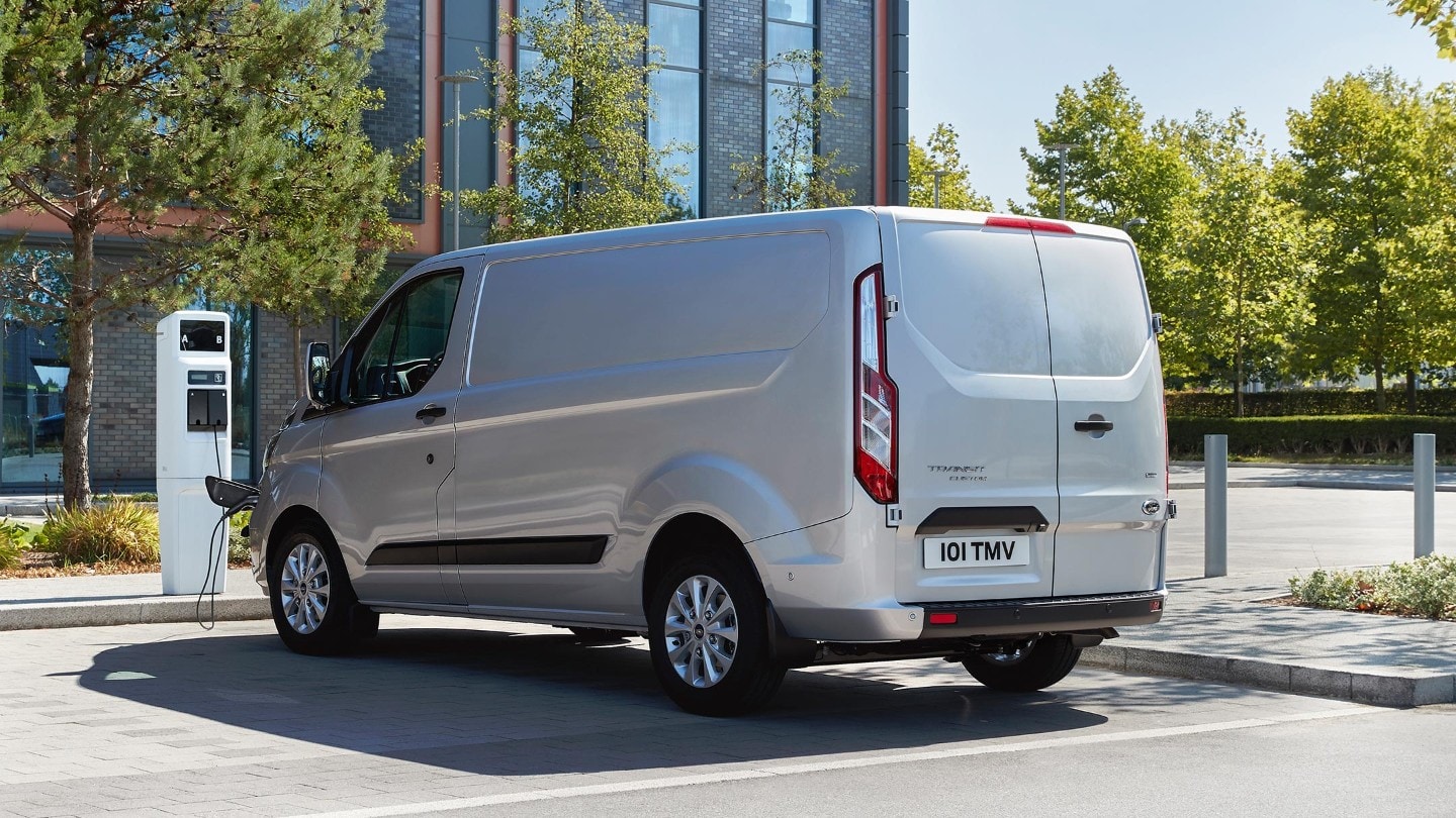 Ford Transit Custom Plug-in-Hybrid Silber Dreiviertel-Heckansicht lädt an Elektro-Tankstelle