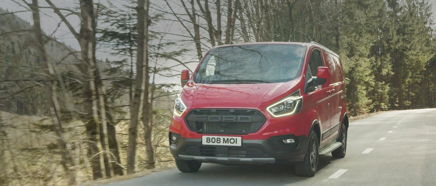 Ford Transit Custom Kastenwagen Trail Rot fährt über Land und auf kurviger Gebirgsstraße