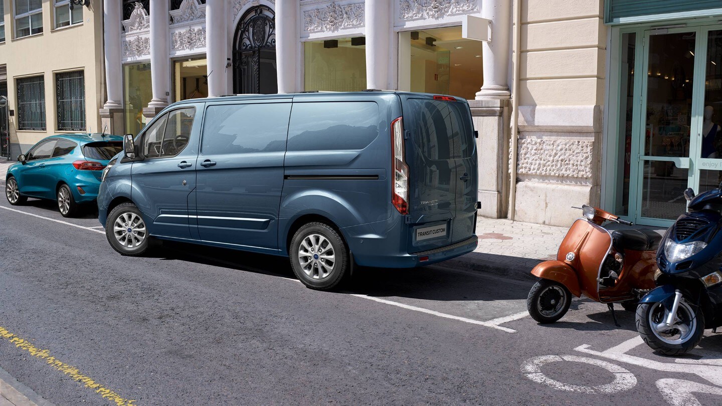 Ford Transit Custom in Blau ¾-Heckansicht parkt rückwärts in Parkbucht ein