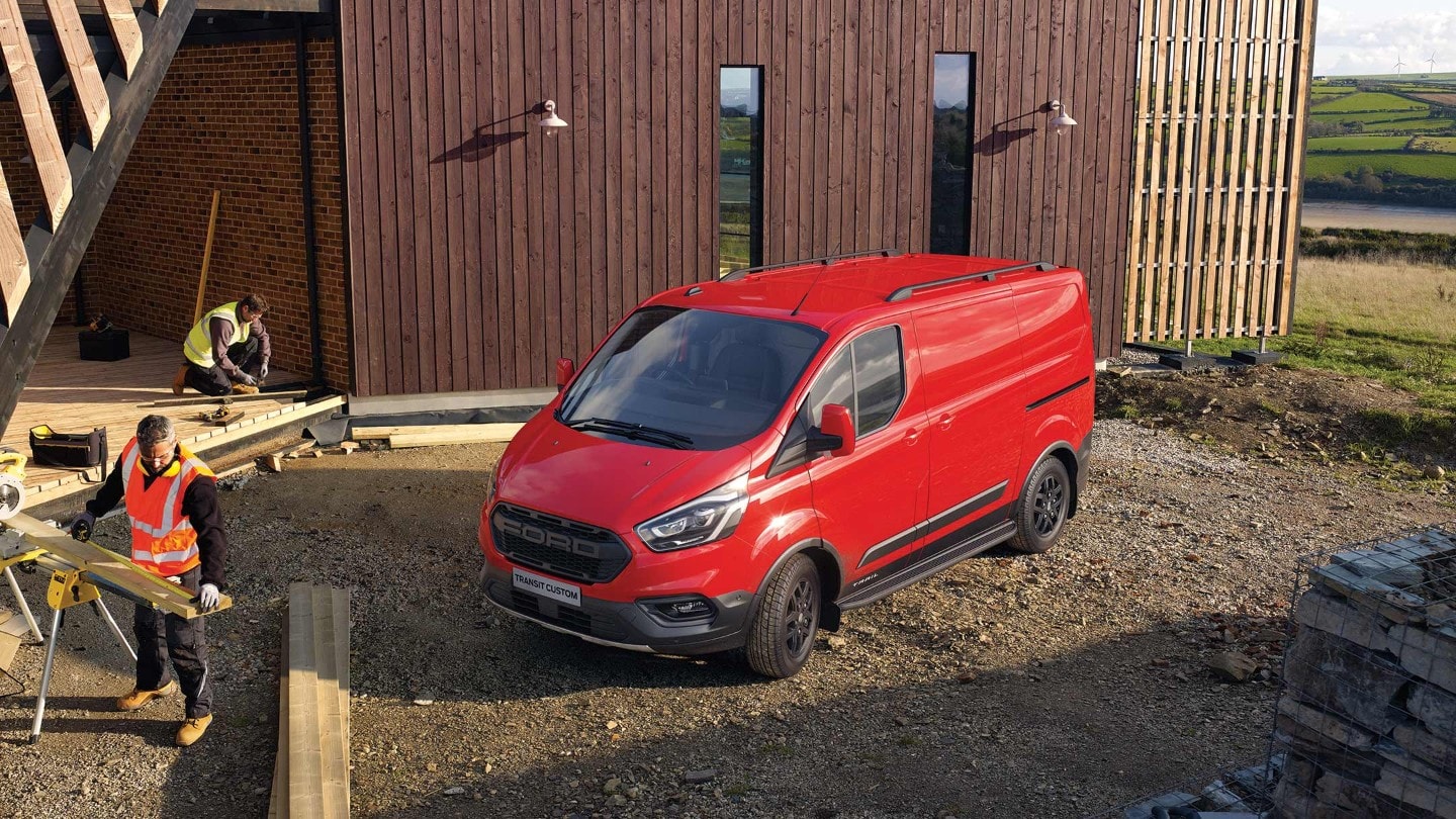 Ford Transit Custom Kastenwagen Trail Rot ¾-Frontansicht parkt vor Neubau