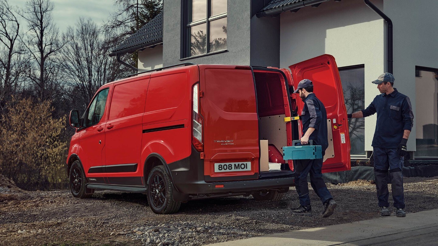 Ford Transit Custom Kastenwagen Trail Rot ¾-Heckansicht parkt in Neubaugebiet und wird beladen
