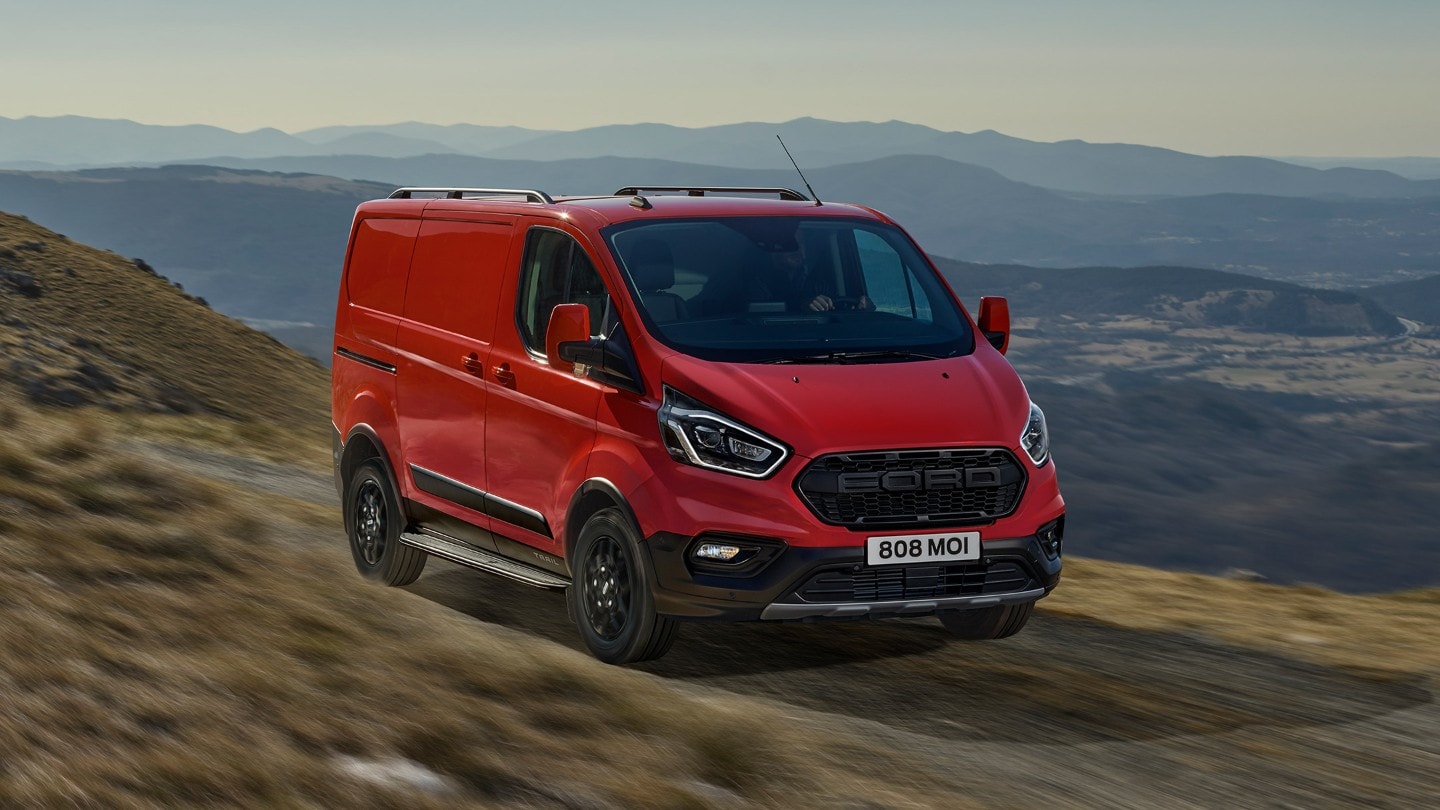 Ford Transit Custom Kastenwagen Trail Rot ¾-Frontansicht fährt auf Feldweg in Gebirge
