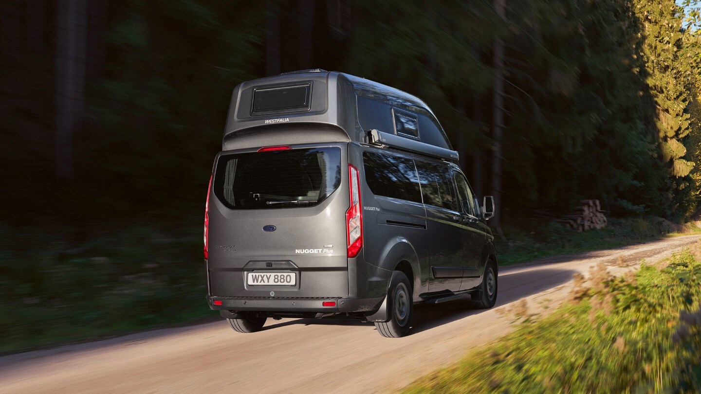 Ford Transit Custom Nugget Plus Anthrazit ¾-Heckansicht in Bewegung auf Waldweg