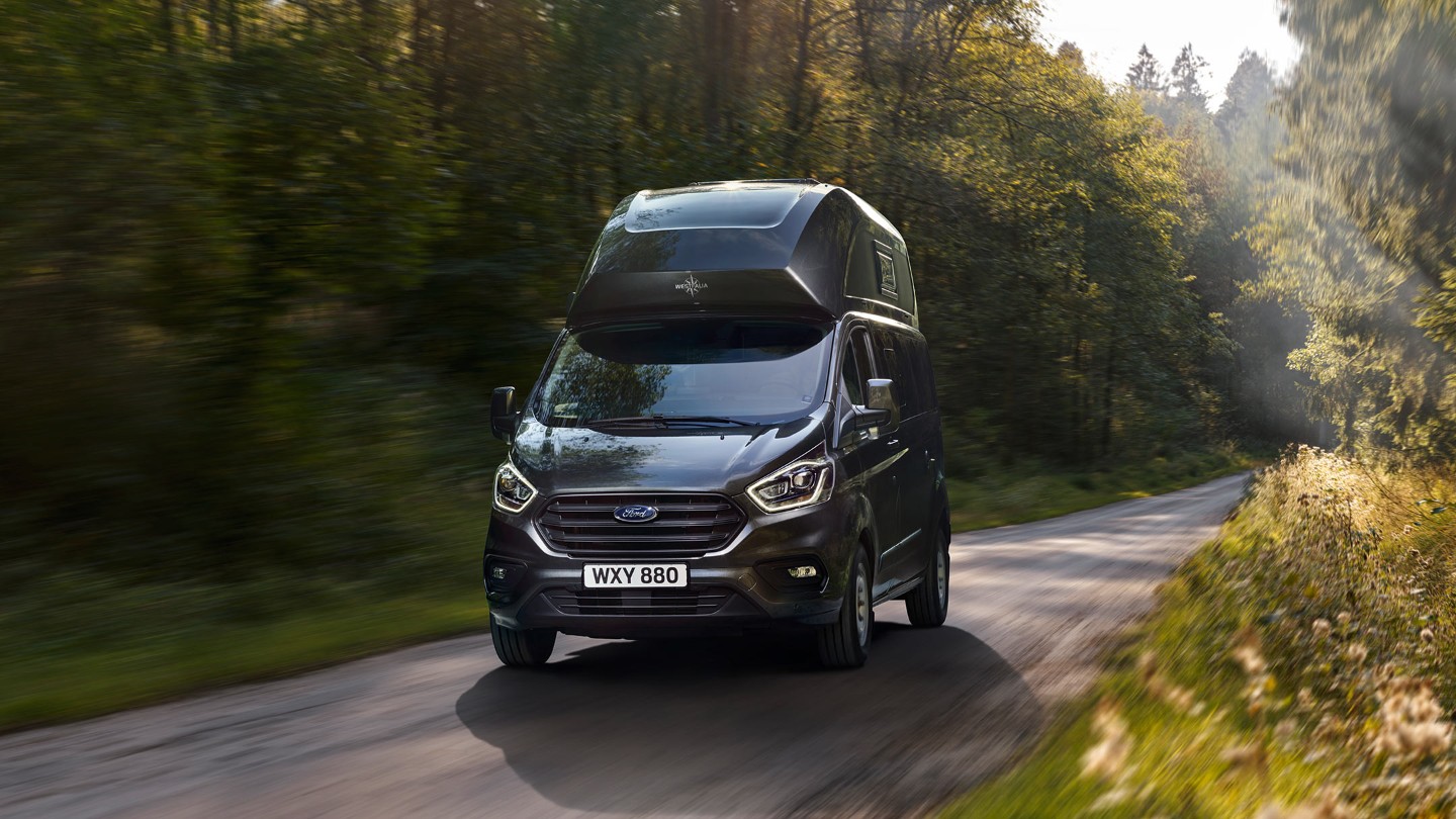 Ford Transit Custom Nugget Plus Schwarz ¾-Frontansicht in Bewegung auf bewaldeter Straße