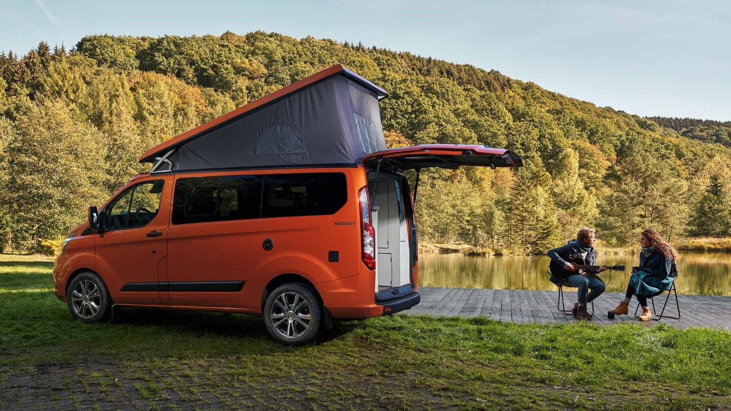Ford Transit Custom Nugget Orange Aufstelldach Seitenansicht parkt auf Wiese an See
