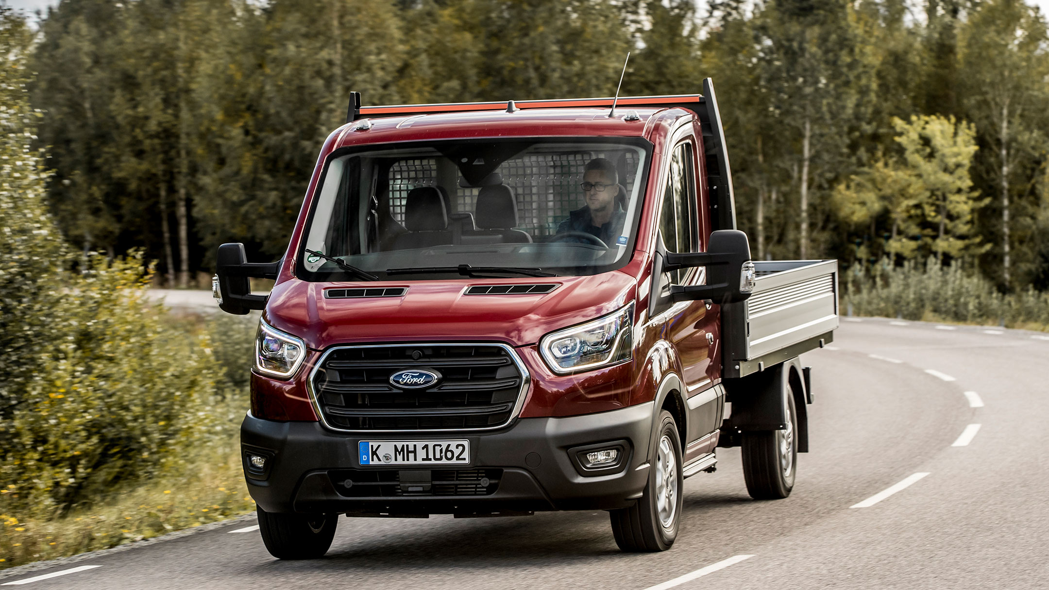 Ford Transit Fahrgestell in Rot ¾ Frontansicht auf Landstraße fahrend