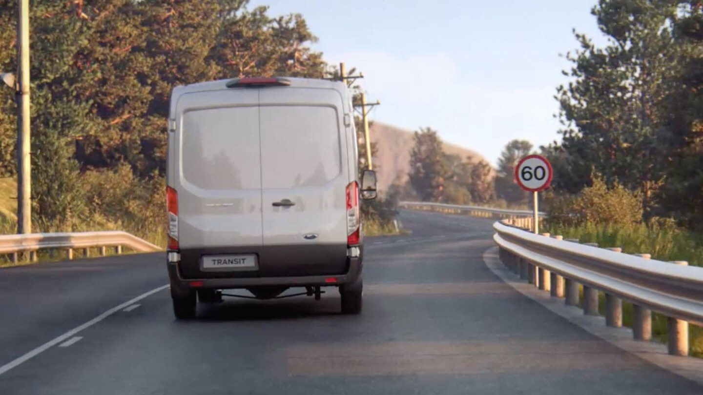 Ford Transit in Silber in der Heckansicht auf Landstraße mit Verkehrsschild fahrend