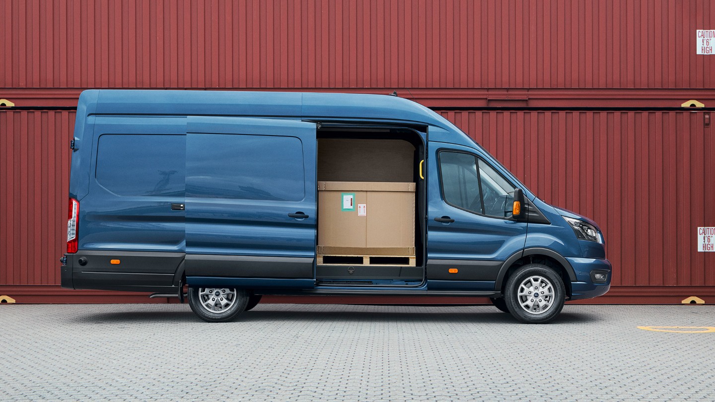 Ford Transit Kastenwagen in Blau Seitenansicht mit geöffneter seitlicher Schiebetüre parkt vor Frachtcontainern