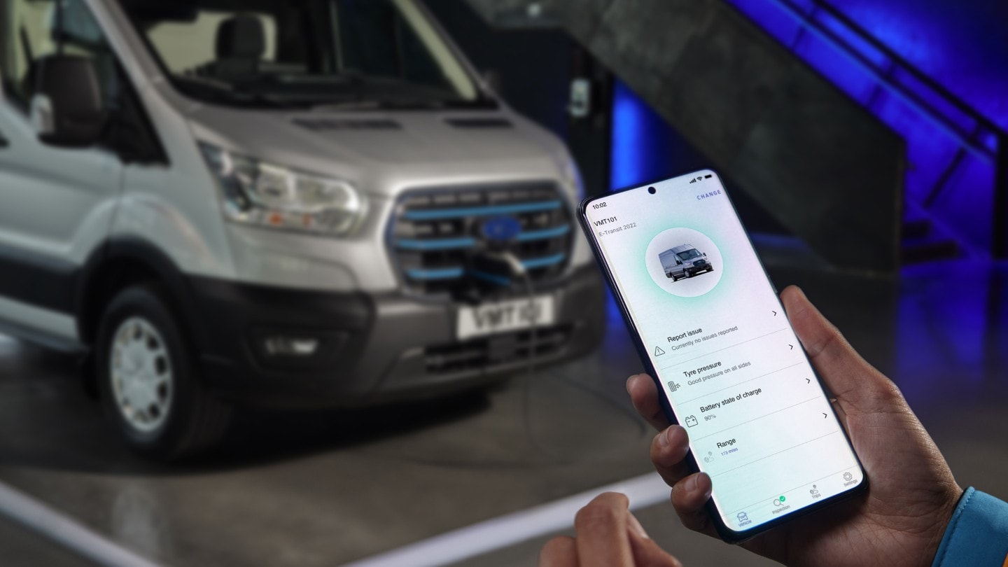 Ford E-Transit in Silber Ausschnitt ¾-Frontansicht und Hand, die Smartphone hält