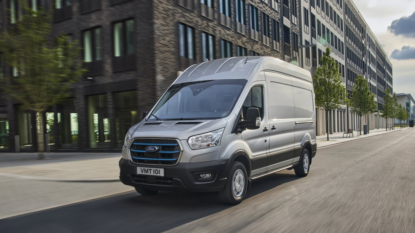 Ford E-Transit silber ¾-Frontansicht fährt durch Stadtgebiet