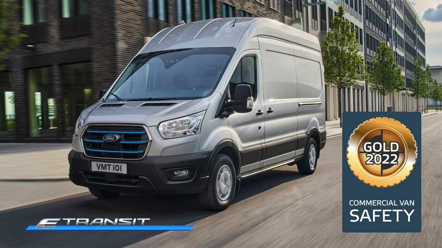 Ford E-Transit Kastenwagen in Silber ¾-Seitenansicht fährt entlang Hochhäusern und NCAP Gold-Logo für Kategorie „Sicherheit“