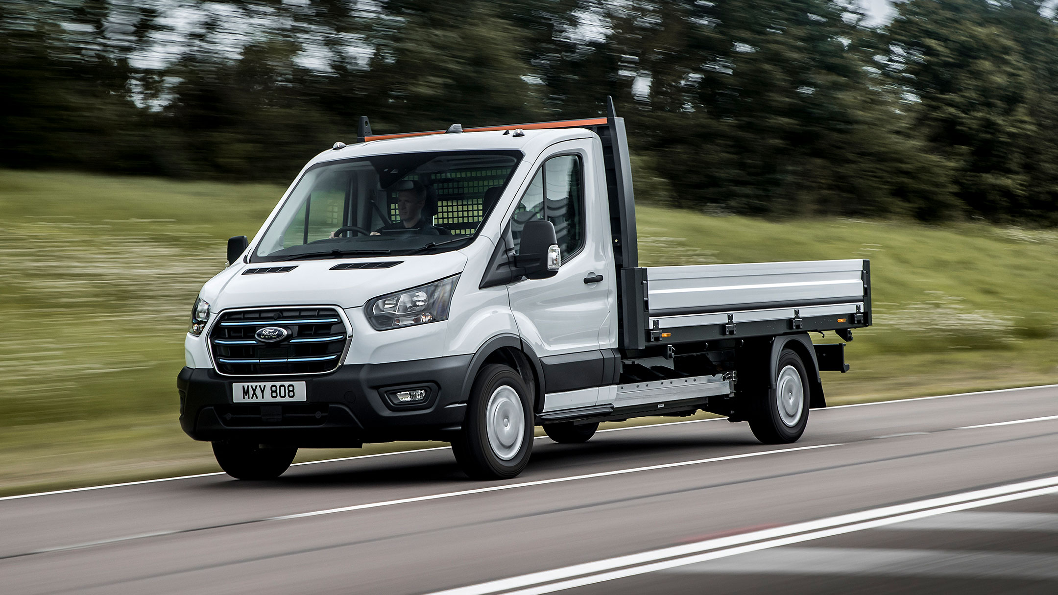 Ford E-Transit Fahrgestell in Weiß in der ¾-Frontansicht auf einer Landstraße fahrend