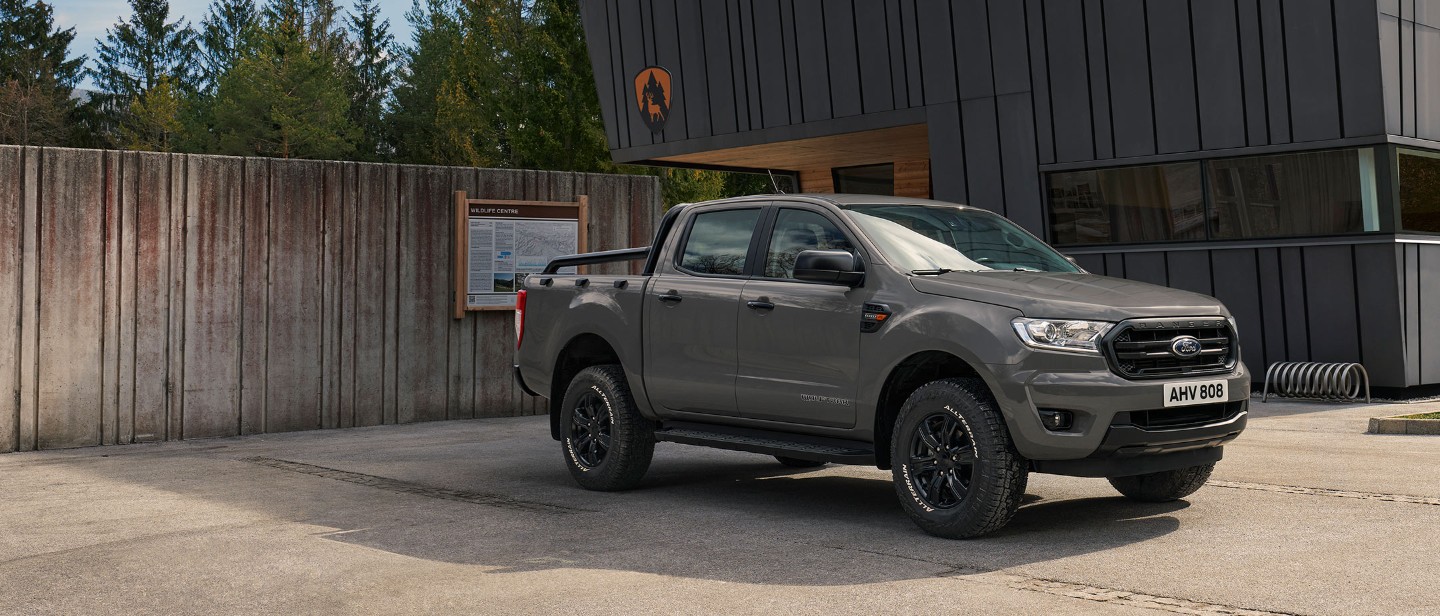 Ford Ranger Wolftrak grau ¾-Seitenansicht parkt vor modernem Gebäude Ford Ranger Wolftrak grau ¾-Seitenansicht parkt vor modernem Gebäude