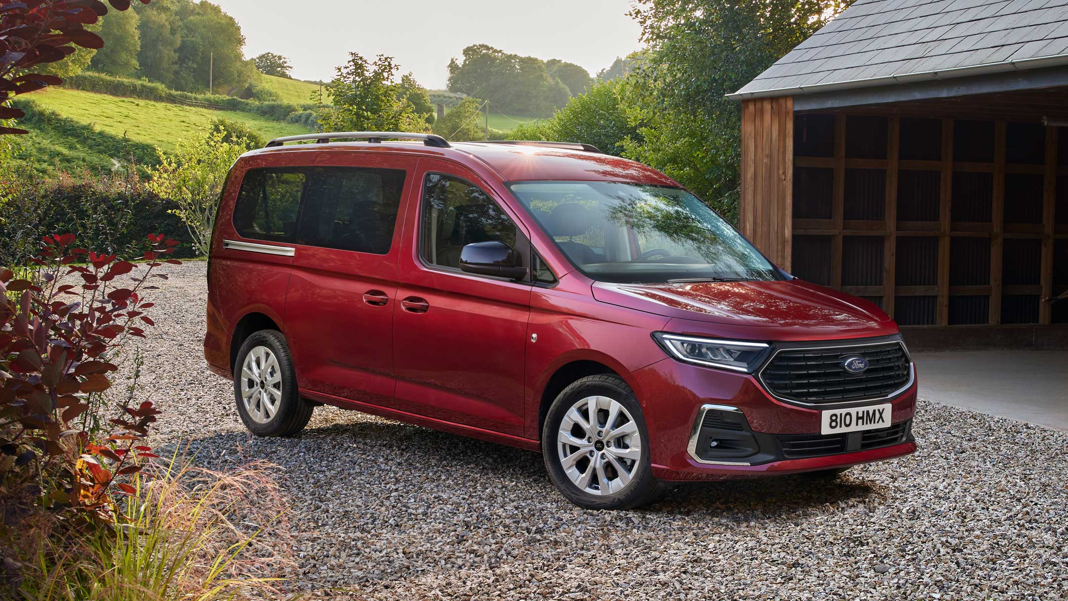 Ford Grand Tourneo Connect in Rot ¾-Frontansicht parkt auf Kiesweg vor Wohnhaus