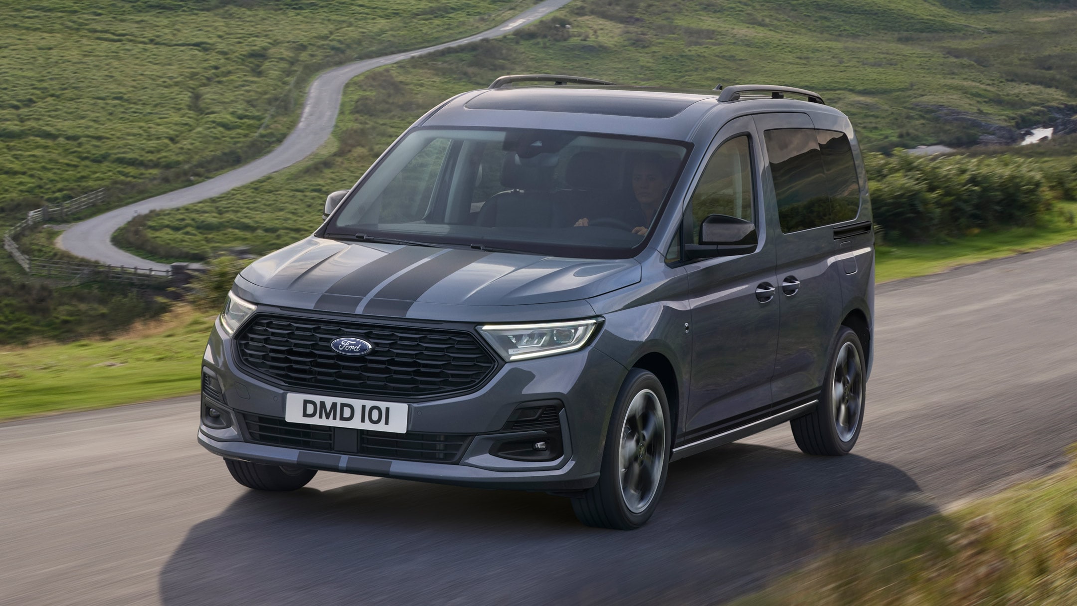 Ford Tourneo Connect in Grau ¾-Frontansicht fährt auf gebirgiger Landstraße mit Fluss im Hintergrund