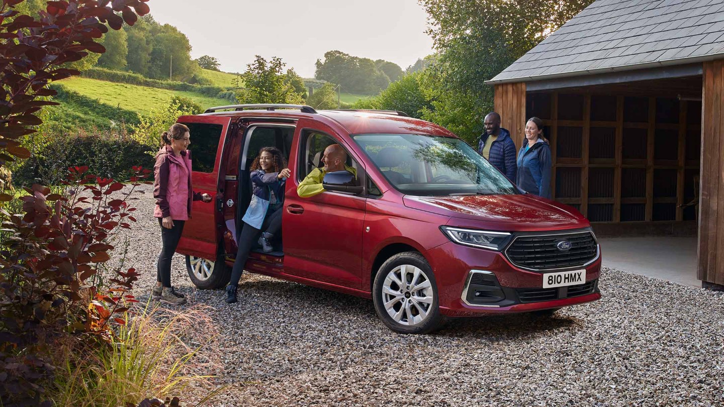 Ford Grand Tourneo Connect in Rot ¾-Frontansicht parkt auf Kiesweg vor Wohnhaus 