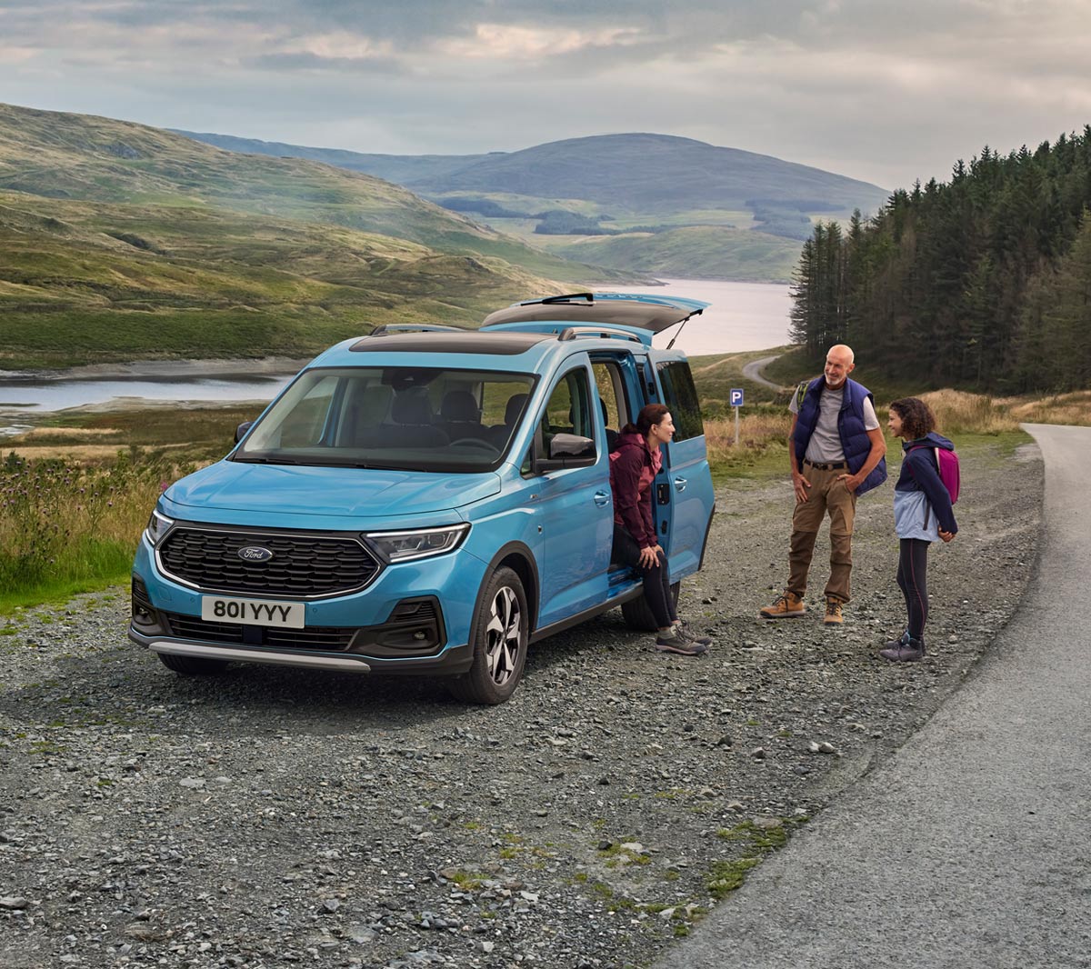 Ford Tourneo Connect Connect in Hellblau ¾-Frontansicht mit geöffneter Schiebetür parkt auf Schotterweg. Frau sitzt im Fahrzeug, Mann und Mädchen stehen daneben