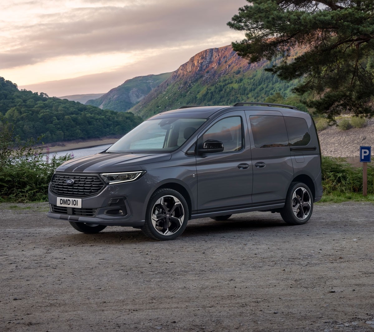 Ford Tourneo Connect in Grau ¾-Frontansicht parkt vor gebirgiger Landschaft mit Fluss im Hintergrund