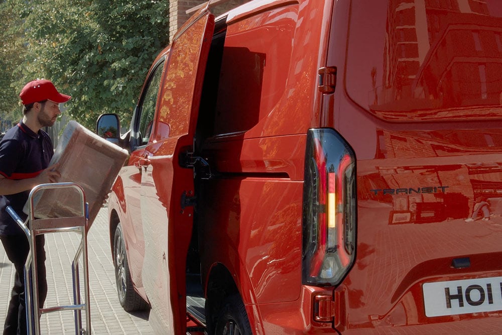 Auslieferer entlädt Pakete aus rotem Ford Transit Custom.