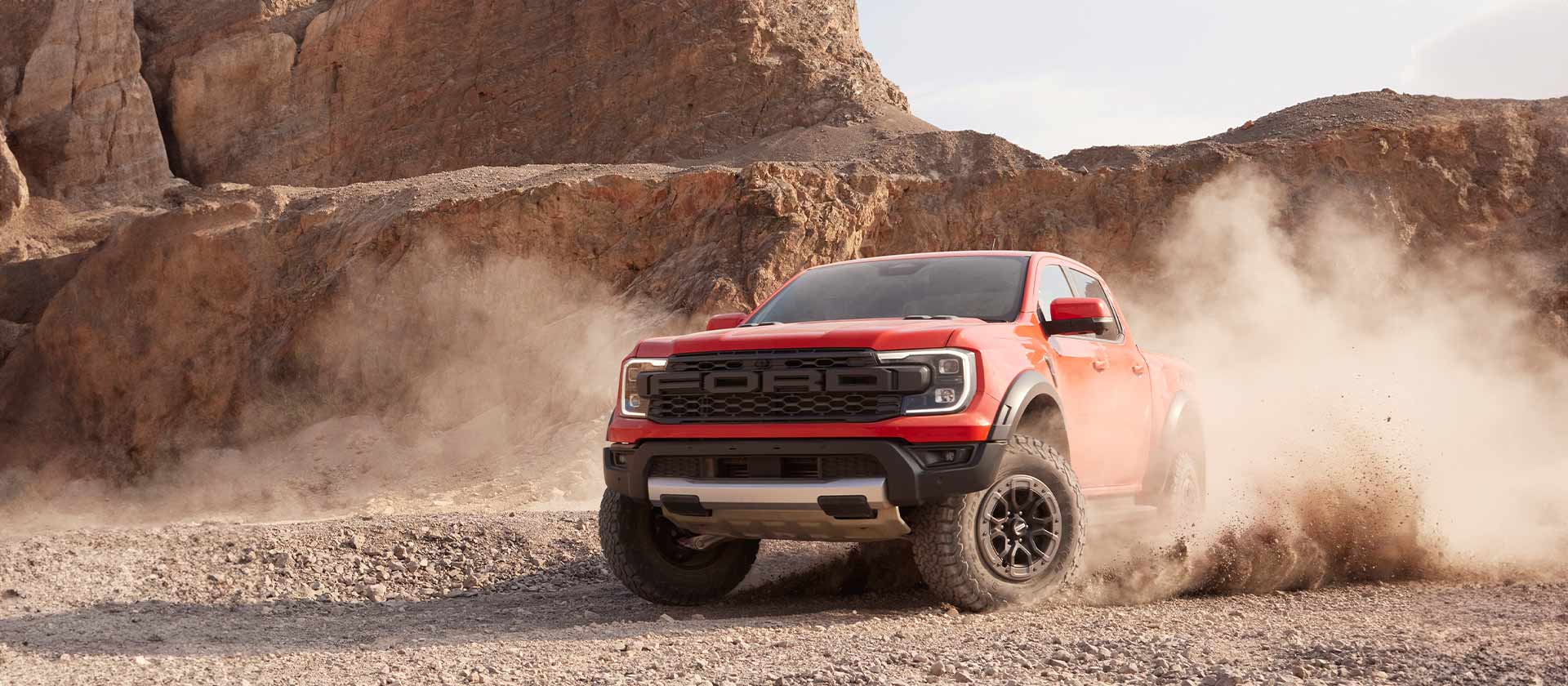 Code Orange Ford Ranger Raptor fährt durch Schotterstaub.