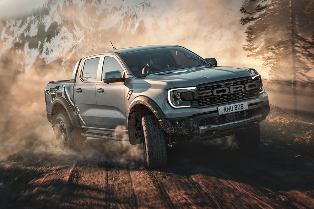 Ein Ford Ranger Raptor im Baja-Modus fährt auf einer unbefestigten Straße durch eine bergige Landschaft.