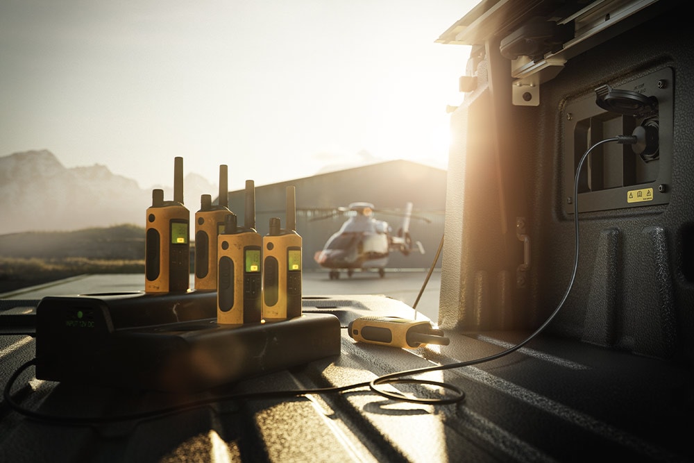 Mehrere Walkie-Talkies werden bei Sonnenuntergang auf der Ladefläche eines Ranger Raptor geladen; im Hintergrund ist ein Hubschrauber zu sehen.