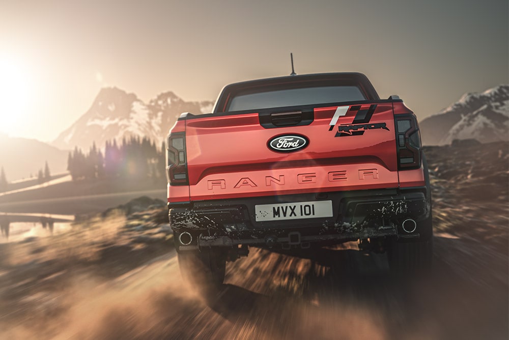 Rückansicht eines roten Ford Ranger Raptor, der auf einer unbefestigten Straße fährt, vor einer Bergkulisse.