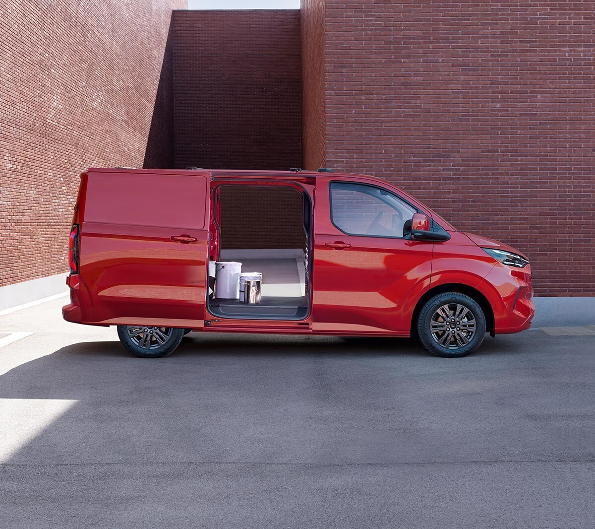 Ford Transit Custom in Rot in der Seitenansicht mit geöffneten seitlichen Schiebetüren parkt vor Backsteingebäude 