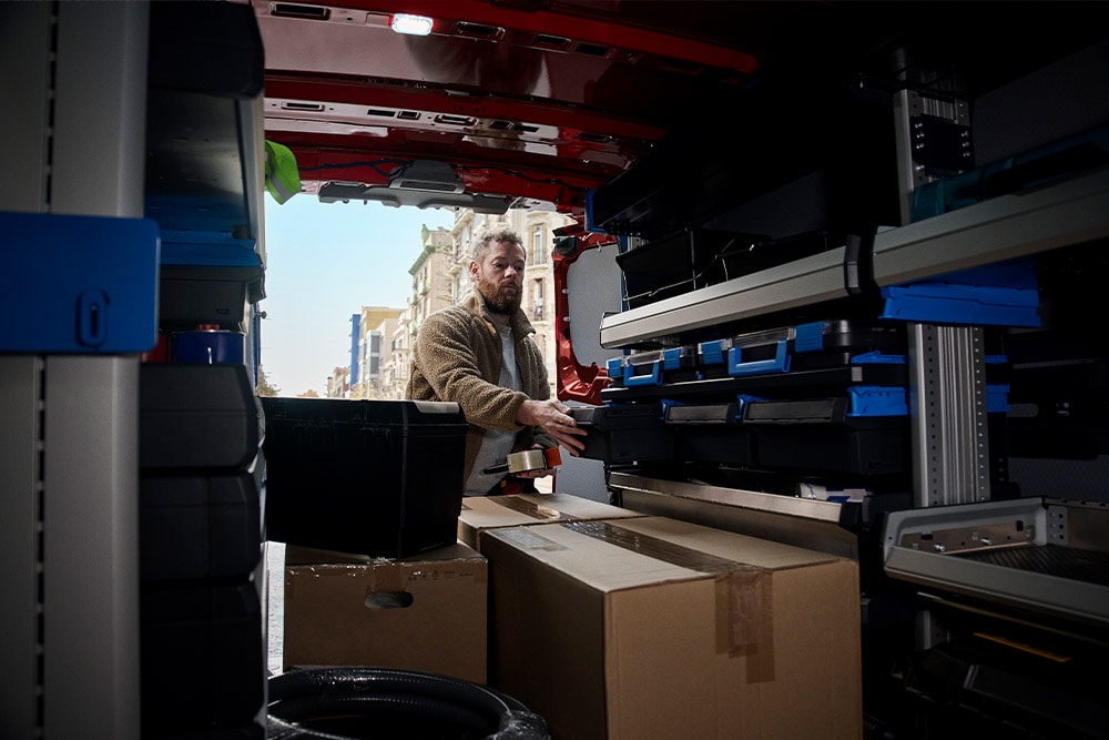 Delivery person unloading packages from the side door of a red Ford Transit Custom.