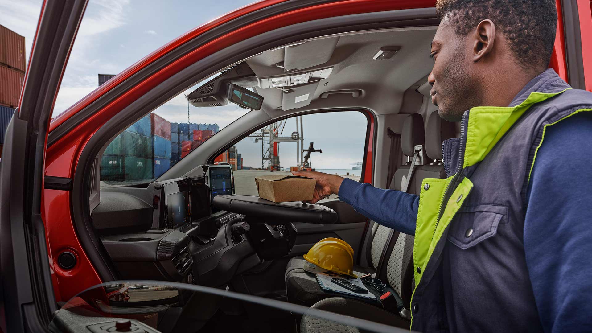 Person legt ein Paket in einen roten Ford Transit Custom