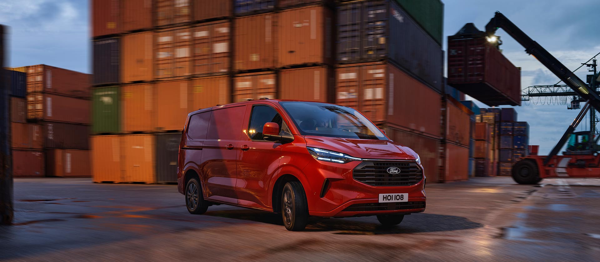 Roter Ford Transit Custom Kleintransporter faehrt durch einen Hafenbereich