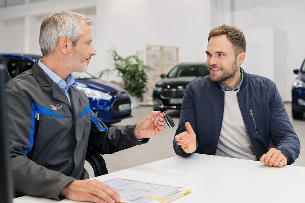 Zwei Personen im Gespräch in einem Ford Autohaus, Beratung zur Finanzierung