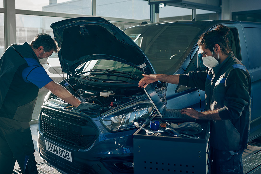 Zwei Mechaniker arbeiten an einem blauen Ford E-Transit Custom Elektro-Transporter.  