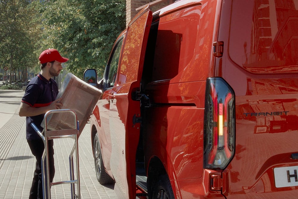 Zusteller laedt Pakete in einen roten Ford Transit Custom