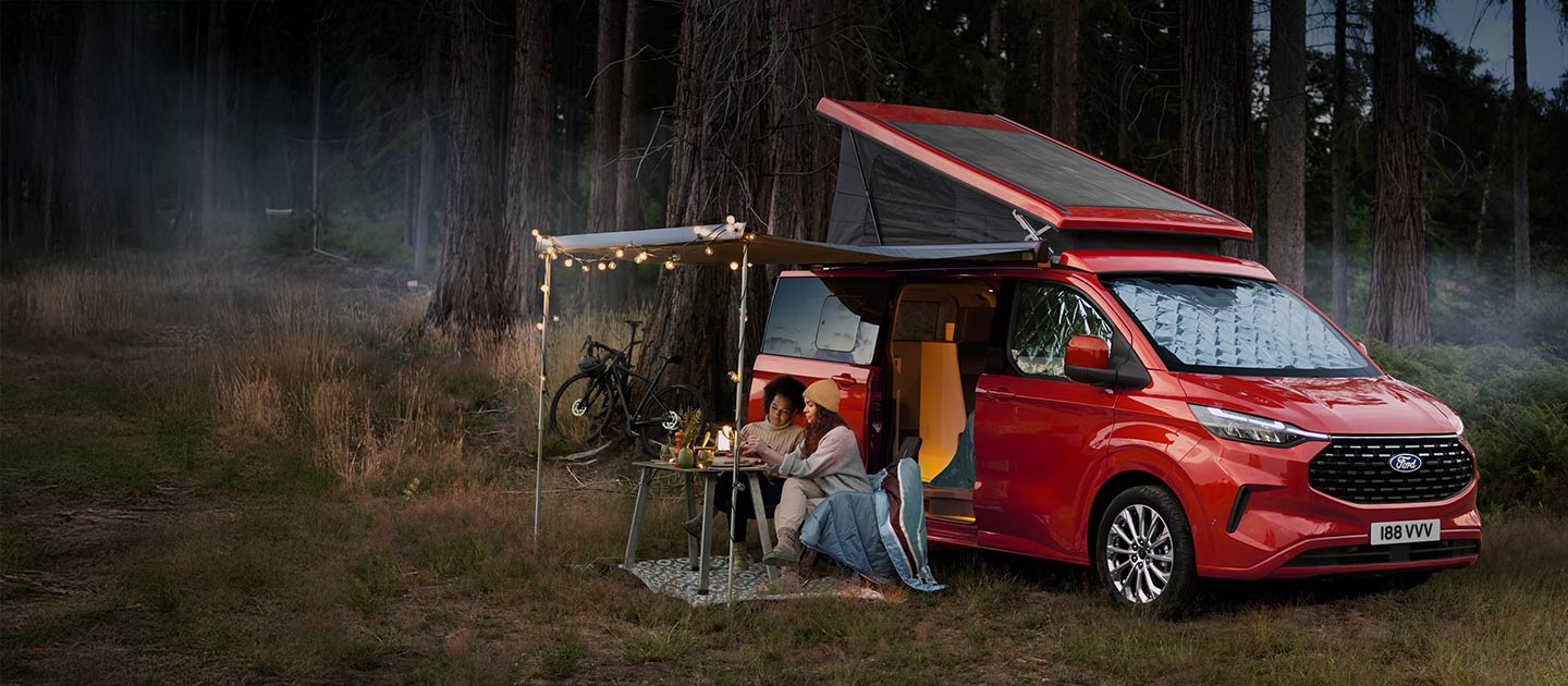 Roter Ford Transit Custom Nugget Camper steht im Wald