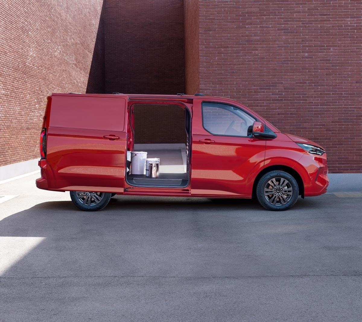 Ford Transit Custom in Rot in der Seitenansicht mit geöffneten seitlichen Schiebetüren parkt vor Backsteingebäude