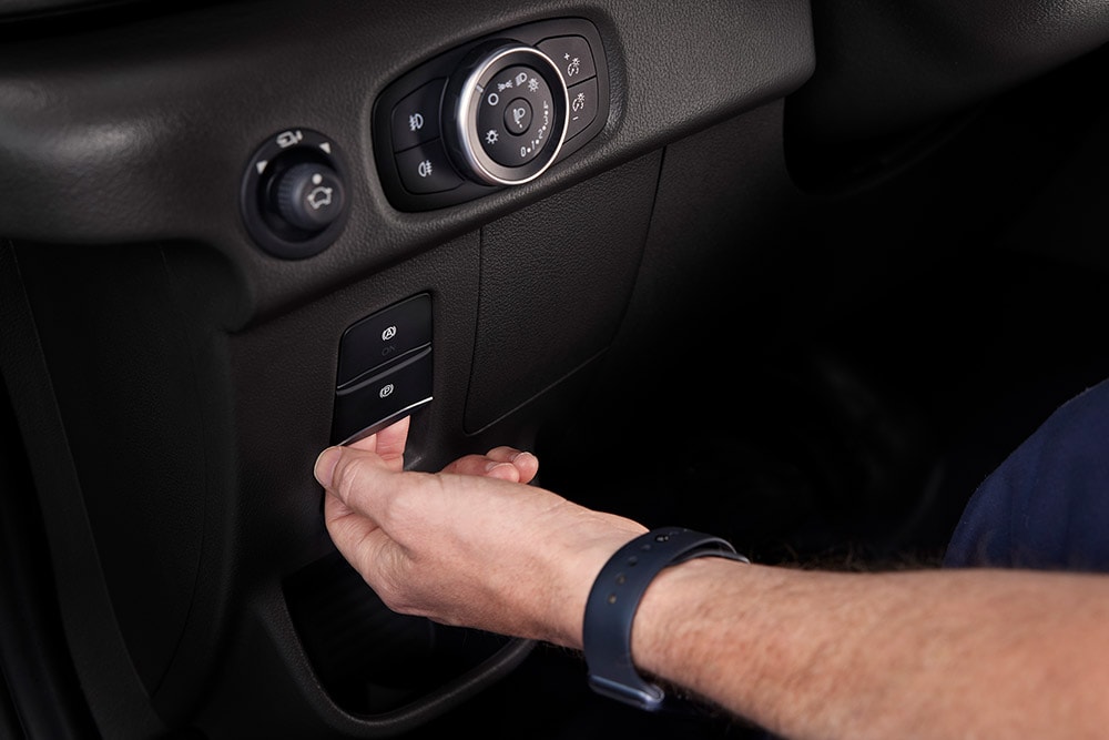 Nahaufnahme einer Hand, die einen Knopf auf dem Armaturenbrett eines Ford E-Transit Kastenwagen drückt.