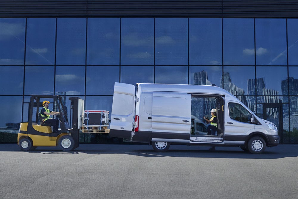 Zwei Personen laden Fracht mit einem Gabelstapler in einen silbernen Ford Transit.