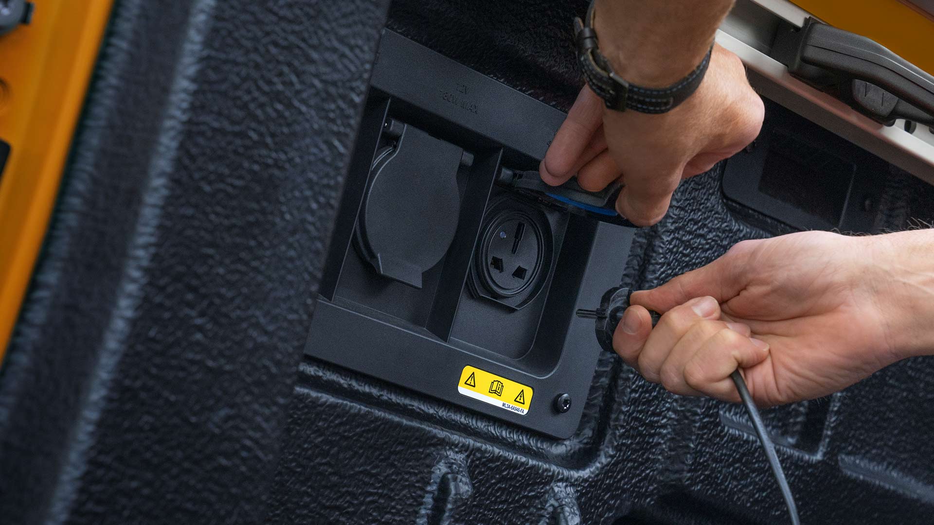 Nahaufnahme von Händen, die Kabel in die Steckdose in der Ladefläche des Ford Ranger stecken.