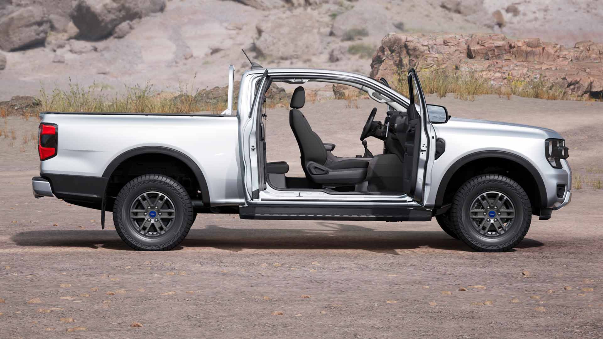 Profilansicht eines silbernen Ford Ranger XLT mit Extrakabine mit offenen Türen, geparkt in staubigem Gelände.