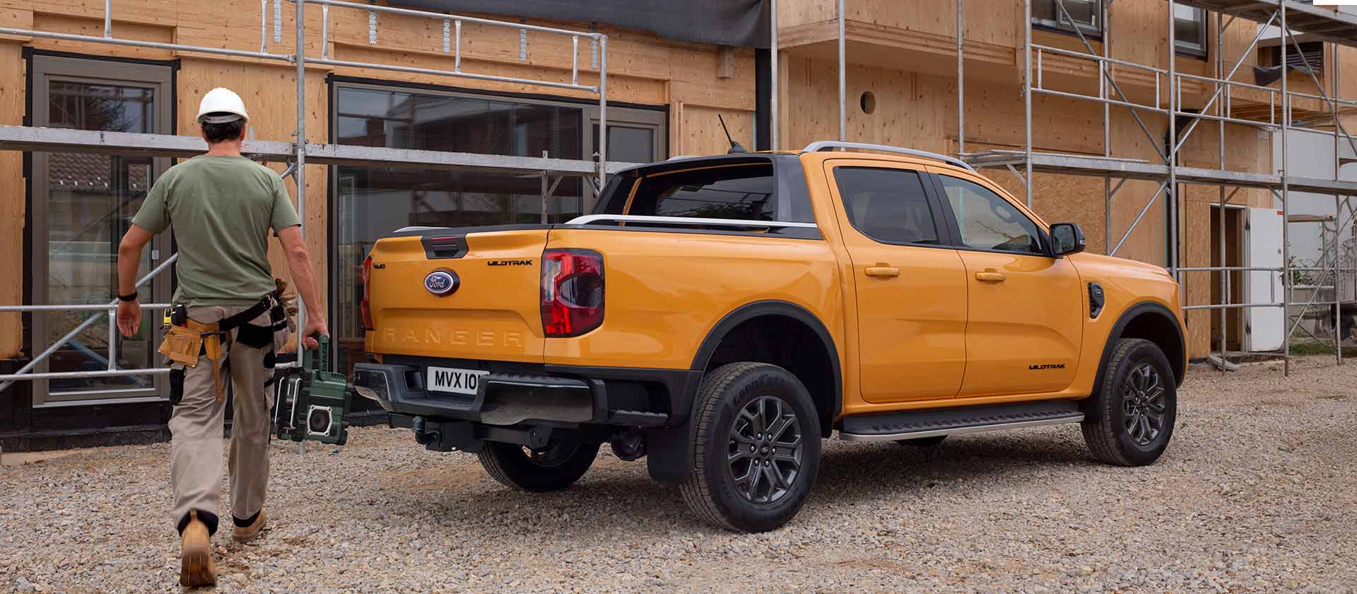 Ein Arbeiter mit Schutzhelm geht auf einer Baustelle auf einen gelben Ford Ranger Pick-up zu.