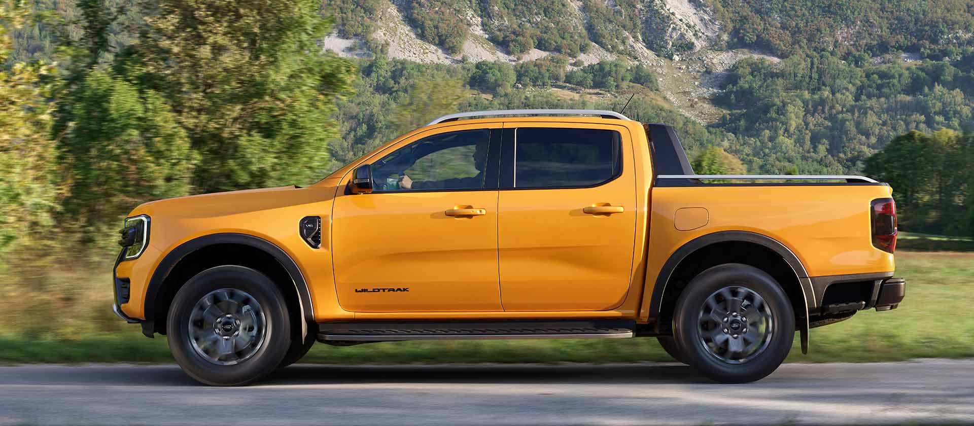 Seitenansicht eines gelben Ford Ranger Wildtrak Doppelkabine, der am Straßenrand in einer Gebirgskulisse parkt.