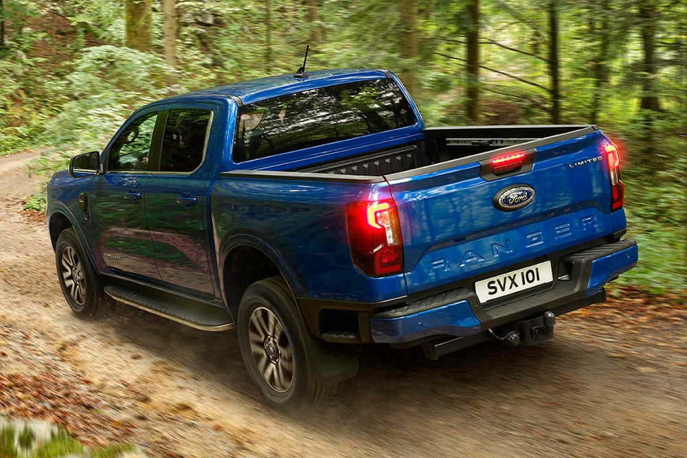 Sicht auf das Rücklicht und die Heckklappe eines blauen Ford Ranger Pick-up-Trucks, der auf einer unbefestigten Straße fährt.