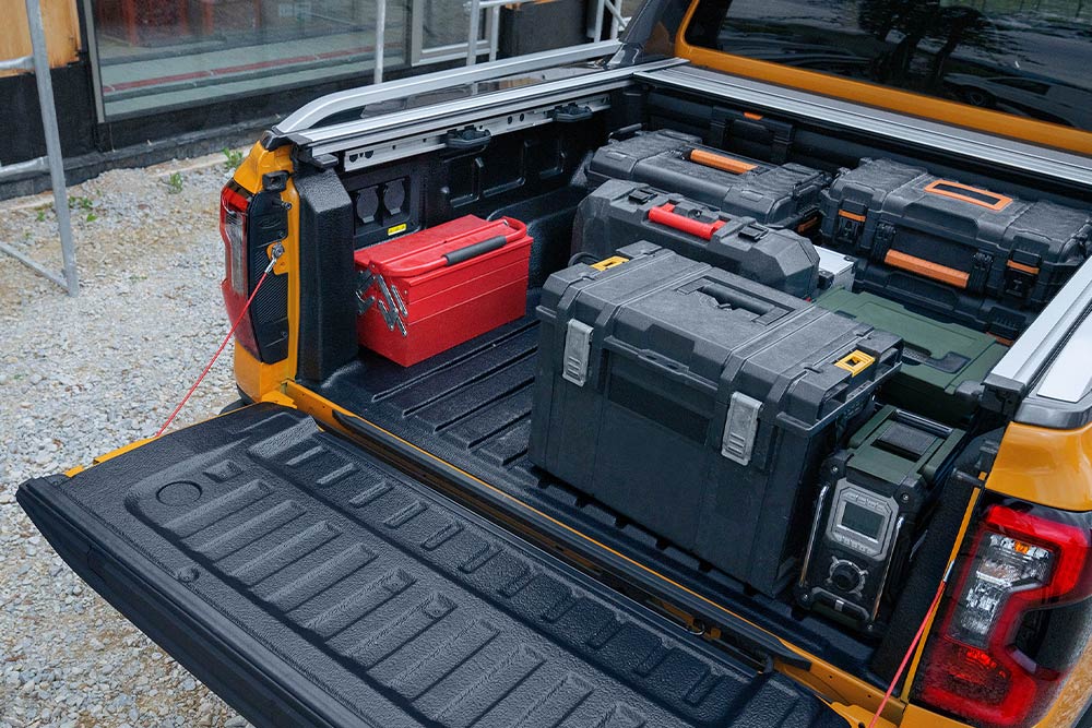 Die Heckklappe eines gelben Ford Ranger in unterer Position, mit einem Holzbrett, das mit einer Klemme befestigt ist.