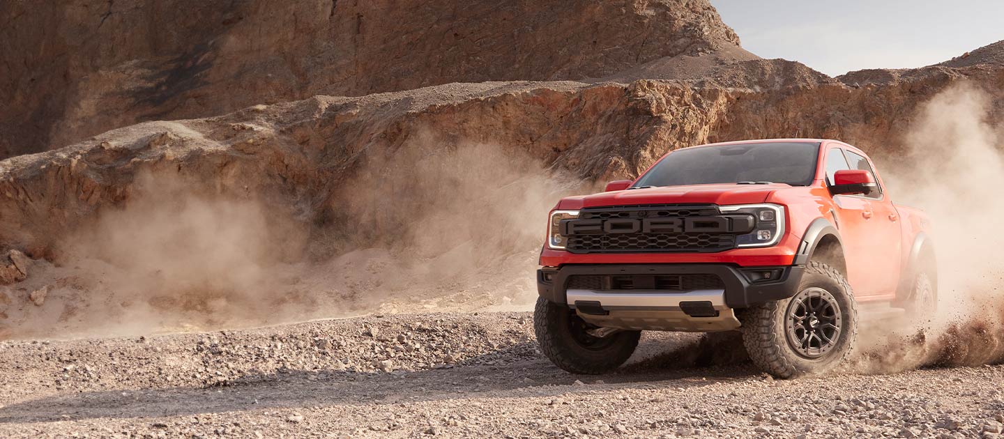 Ein roter Ford Ranger Raptor wirbelt Staub auf, während er durch eine Wüstenlandschaft fährt.