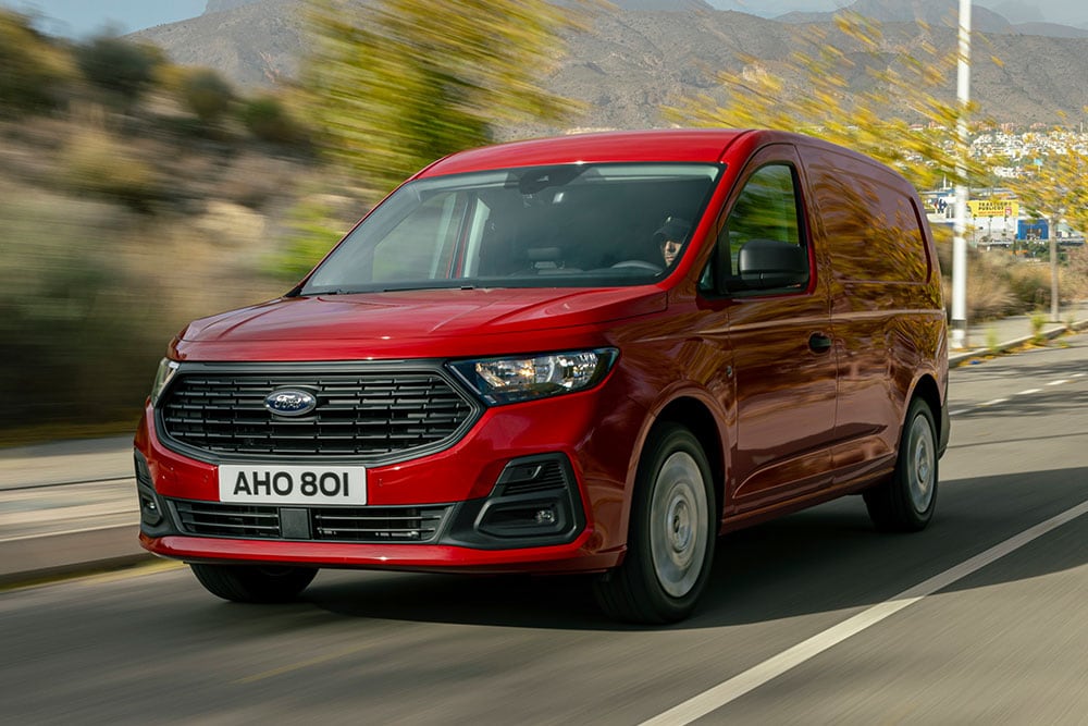 Ein Ford Transit Connect fährt auf einer Straße; gut sichtbar sind der Kühlergrill und die Scheinwerfer.