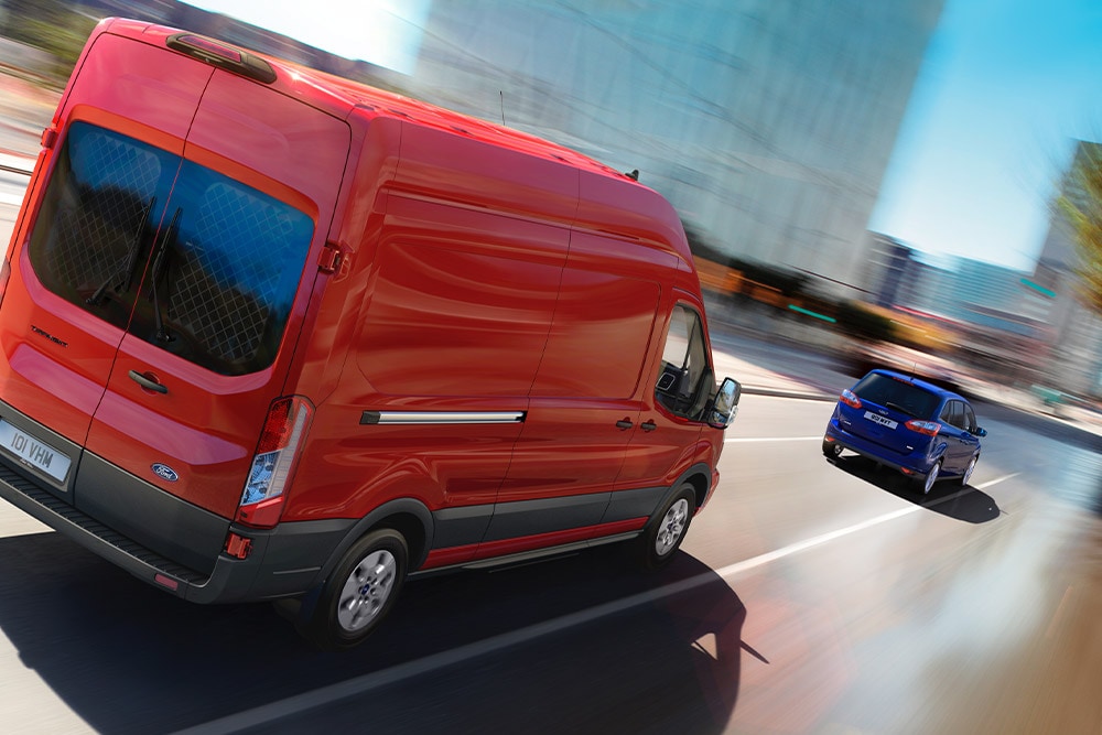 Roter Ford Transit Kastenwagen fährt auf einer Straße.