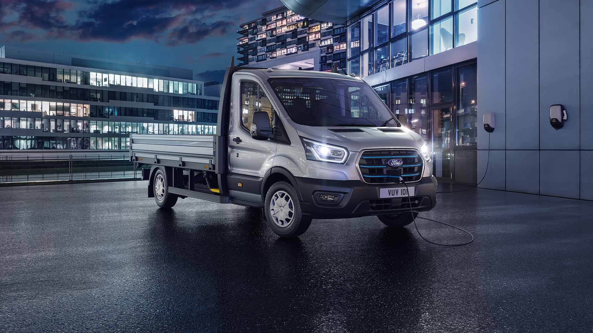 Ford Transit Fahrgestell in Silber bei Nacht vor einem modernen Gebäude geparkt.