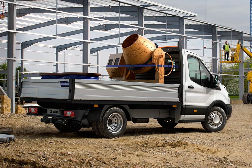 Ein Ford Transit Fahrgestell Einzelkabine mit einem Betonmischer auf der Ladefläche parkt auf einer Baustelle. 